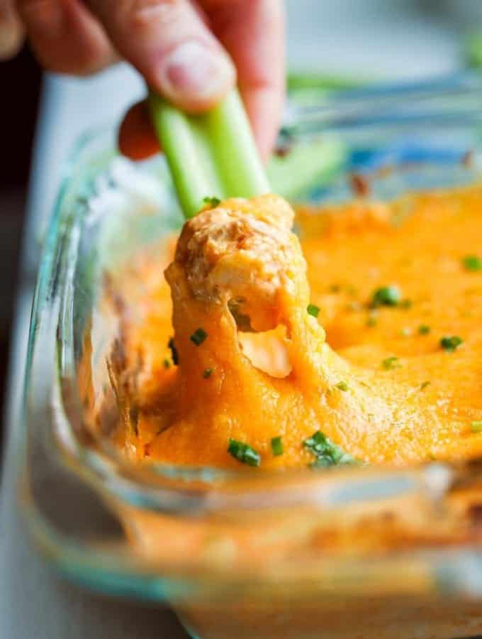 Low carb buffalo chicken wing dip being pulled out of a tray with celery.