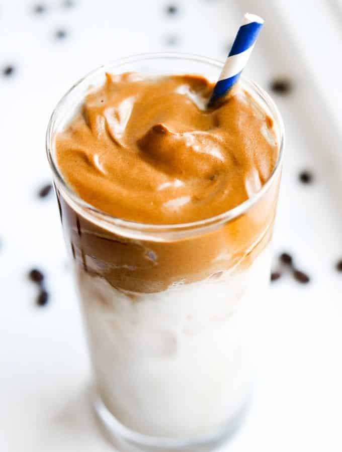 A glass of dalgona coffee with a blue straw in the glass.