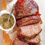 A meatloaf covered in ketchup cut into slices with spices next to it.