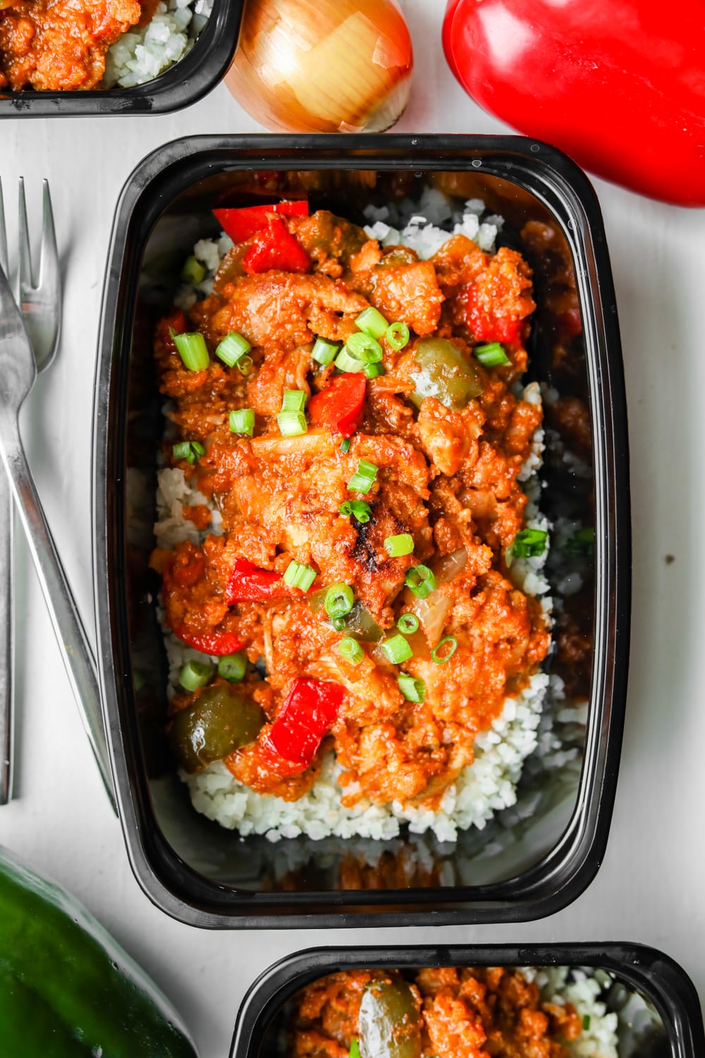 A serving of low carb BBQ chicken and vegetables next to a red pepper, a green pepper, a yellow onion, and a couple of forks.