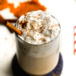 A clear glass cup filled with a pumpkin spice latte that's been topped with whipped cream and spices.