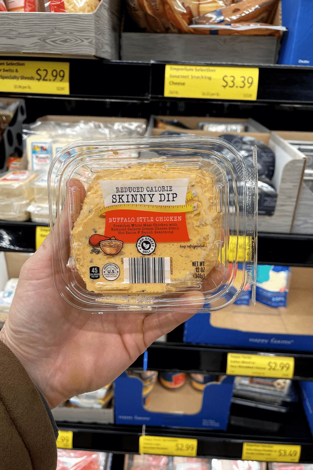 A hand holding a package of buffalo chicken dip.