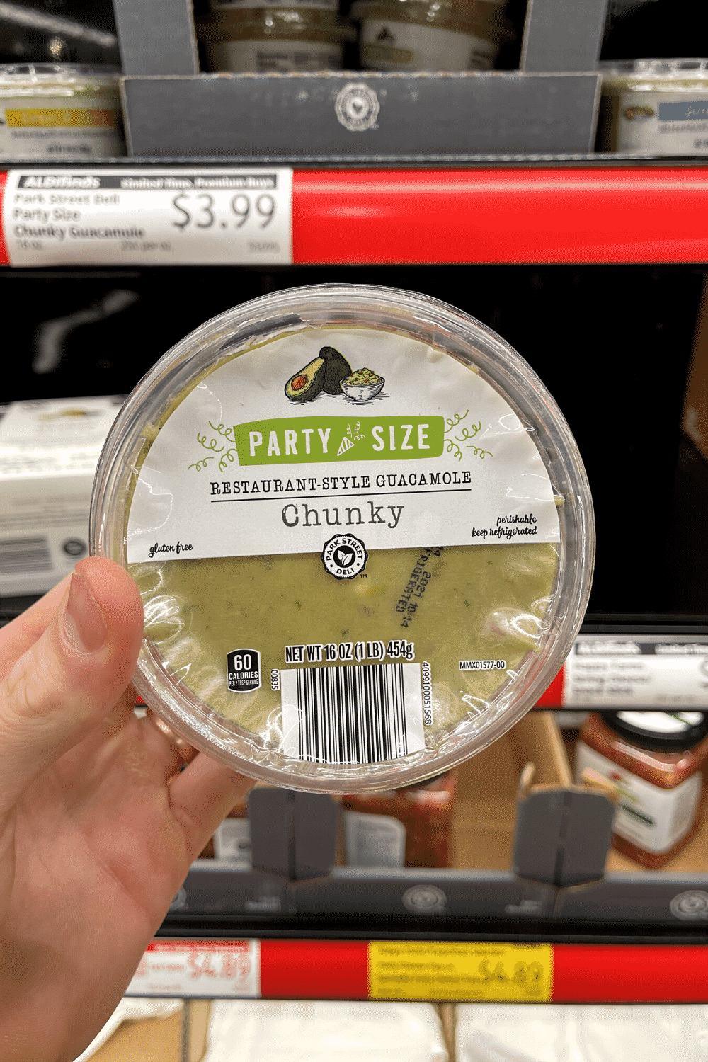 A hand holding a container of guacamole.