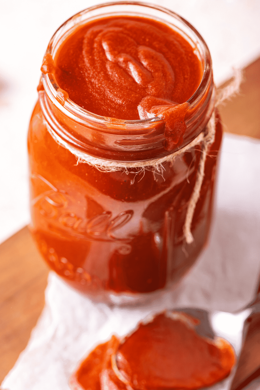 A glass jar filled to the top with BBQ sauce. Some barbecue sauce is dripping over the front edge of the jar.