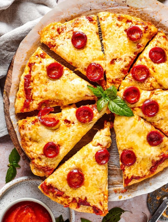 A cheese and pepperoni chicken crust pizza cut into 8 slices on a piece of parchment paper on a pizza tray.