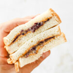 A hand holding a peanut butter and jelly sandwich that's been cut in half.