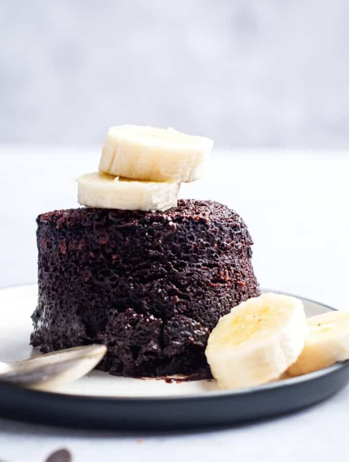 Two banana slices on top of a chocolate protein mug cake and a white plate.