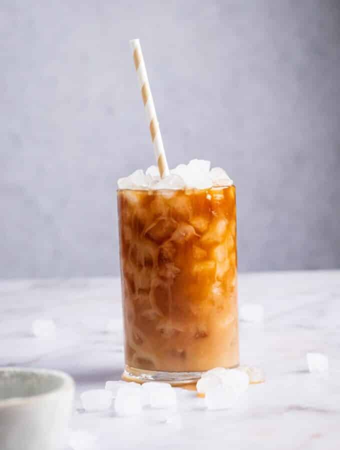 A glass of protein coffee on a white counter with ice cubes on it.
