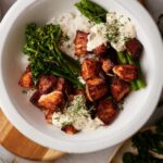 Air fryer salmon bites rice bowl. The bowl is filled with white rice topped with steamed asparagus and broccolini on either side with dollops of dill sauce and a generous serving of air fried salmon bites.