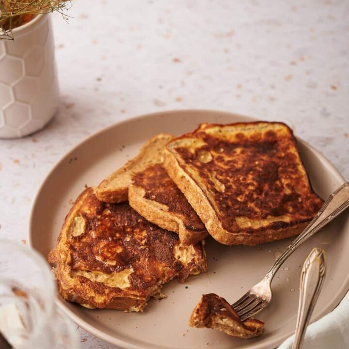 Three french toast slices arranged on a plate with a fork holding a piece of one of the french toasts.