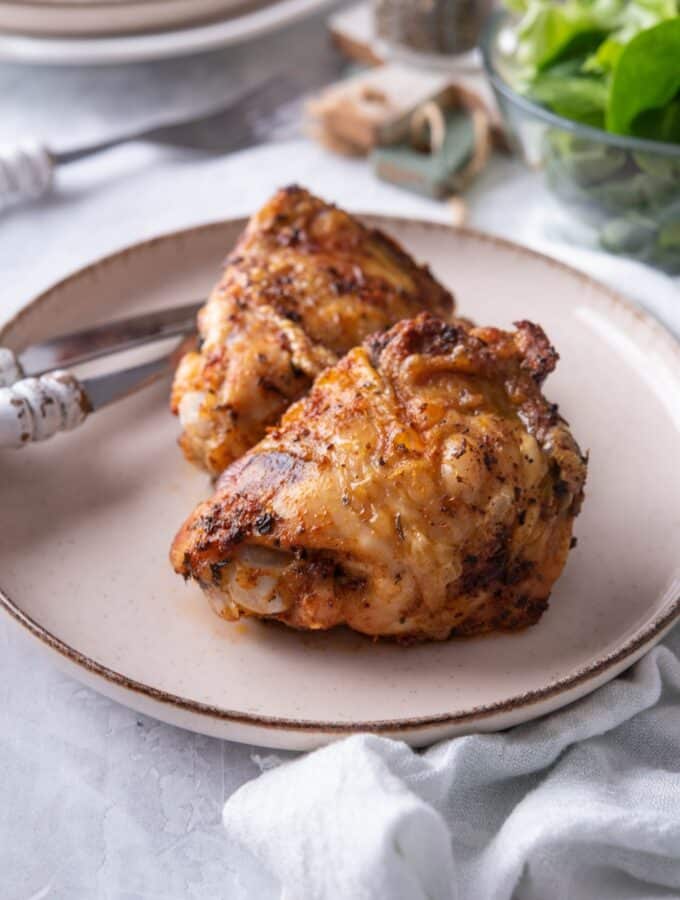 Close up of air fryer chicken thighs on a plate with a knife and fork.
