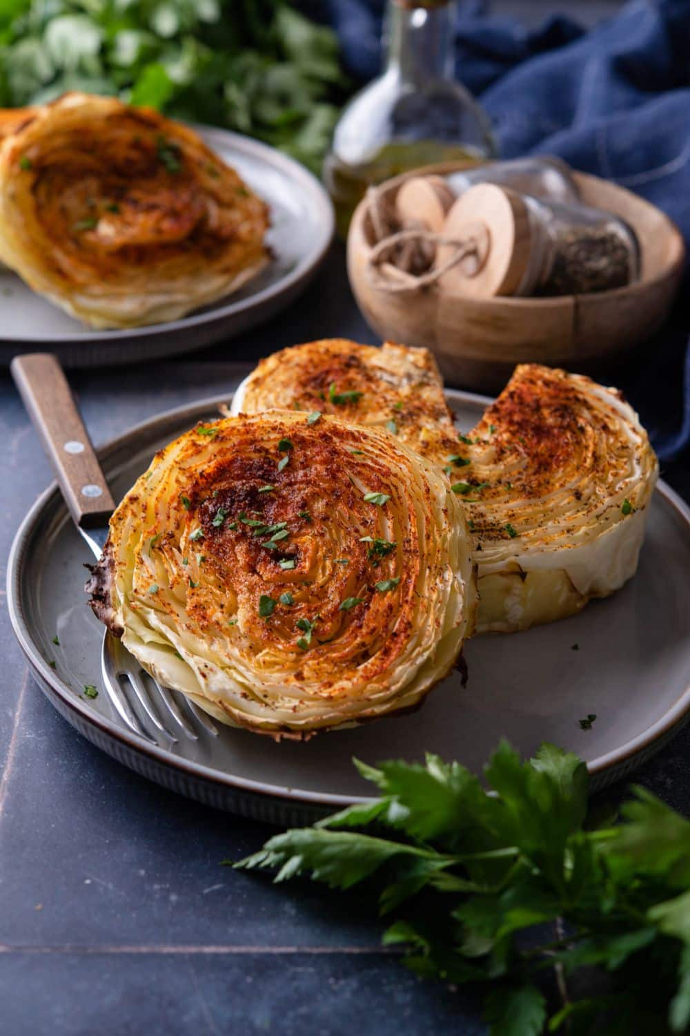 Two cabbage steaks on a plate, one with a piece taken out. A second plate of cabbage steaks sits to the side.