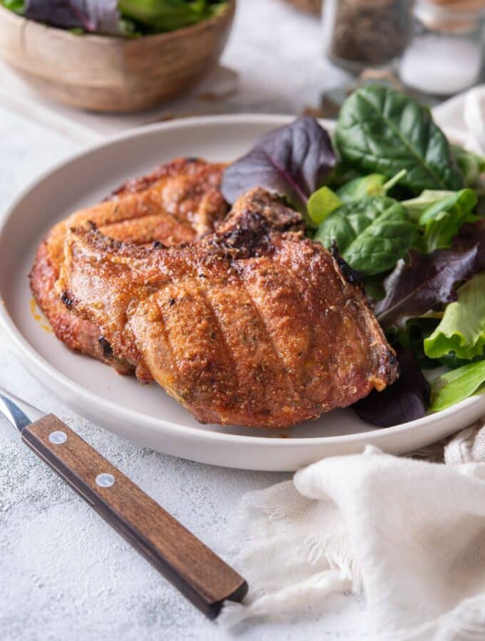 Two broiled bone-in pork chops with a side of salad greens on a plate.
