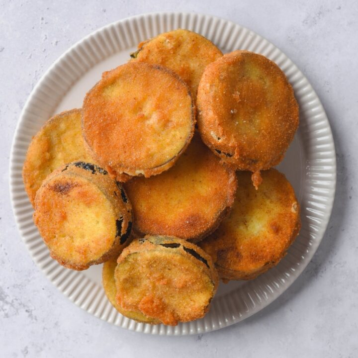 A bunch of fried eggplant slices on top of a white plate on a counter.