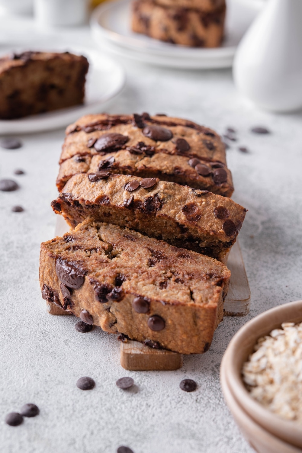 A sliced loaf of chocolate chip oatmeal banana bread on a wood cutting board. Behind are more plate of banana bread slices.