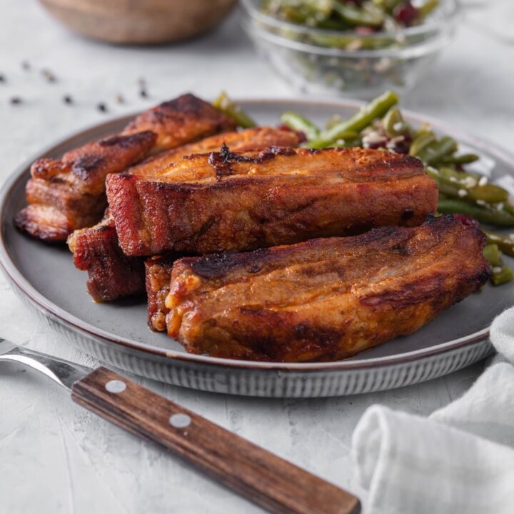 Roasted pork belly strips on a plate served with green bean salad. In the back is a small bowl of green bean salad.