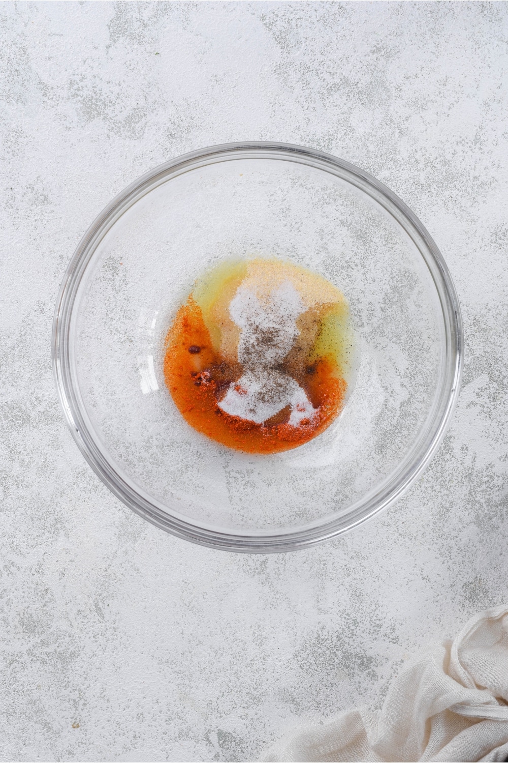 Glass bowl of olive oil, garlic powder, onion powder, paprika, salt, and pepper.