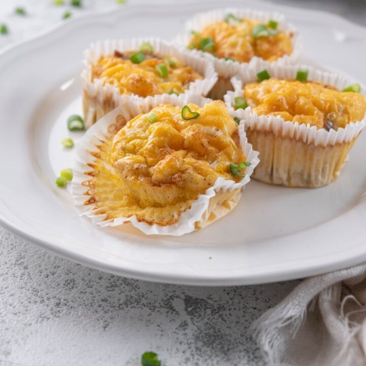 Four sausage egg muffins in muffin liners on a white plate, one partially opened.