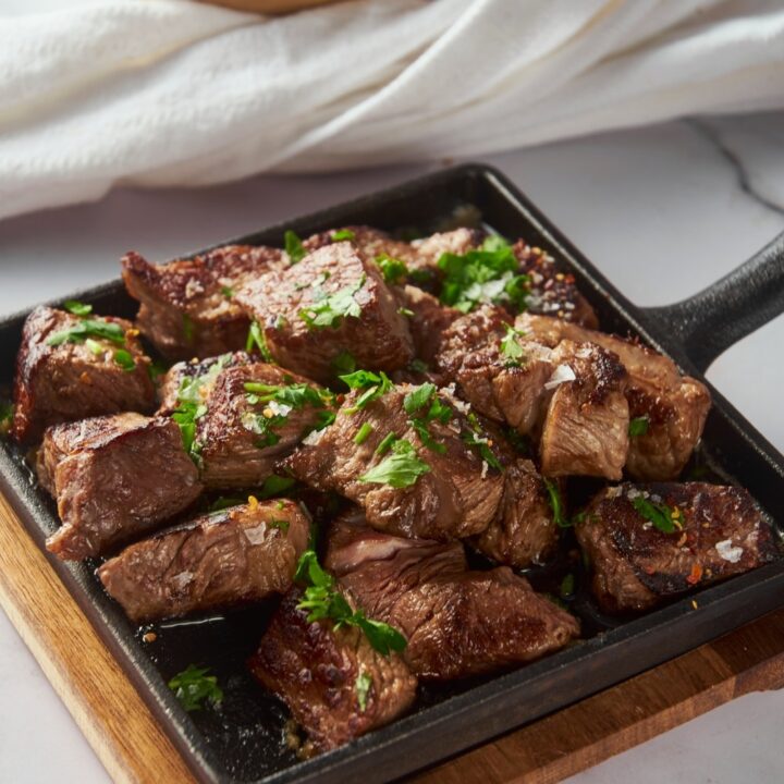 Garlic steak bites on a cast iron pan garnished with parsley.