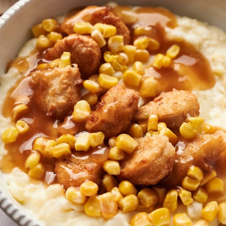 A KFC bowl filled with mashed potatoes, chicken nuggets, corn kernels, and brown gravy.