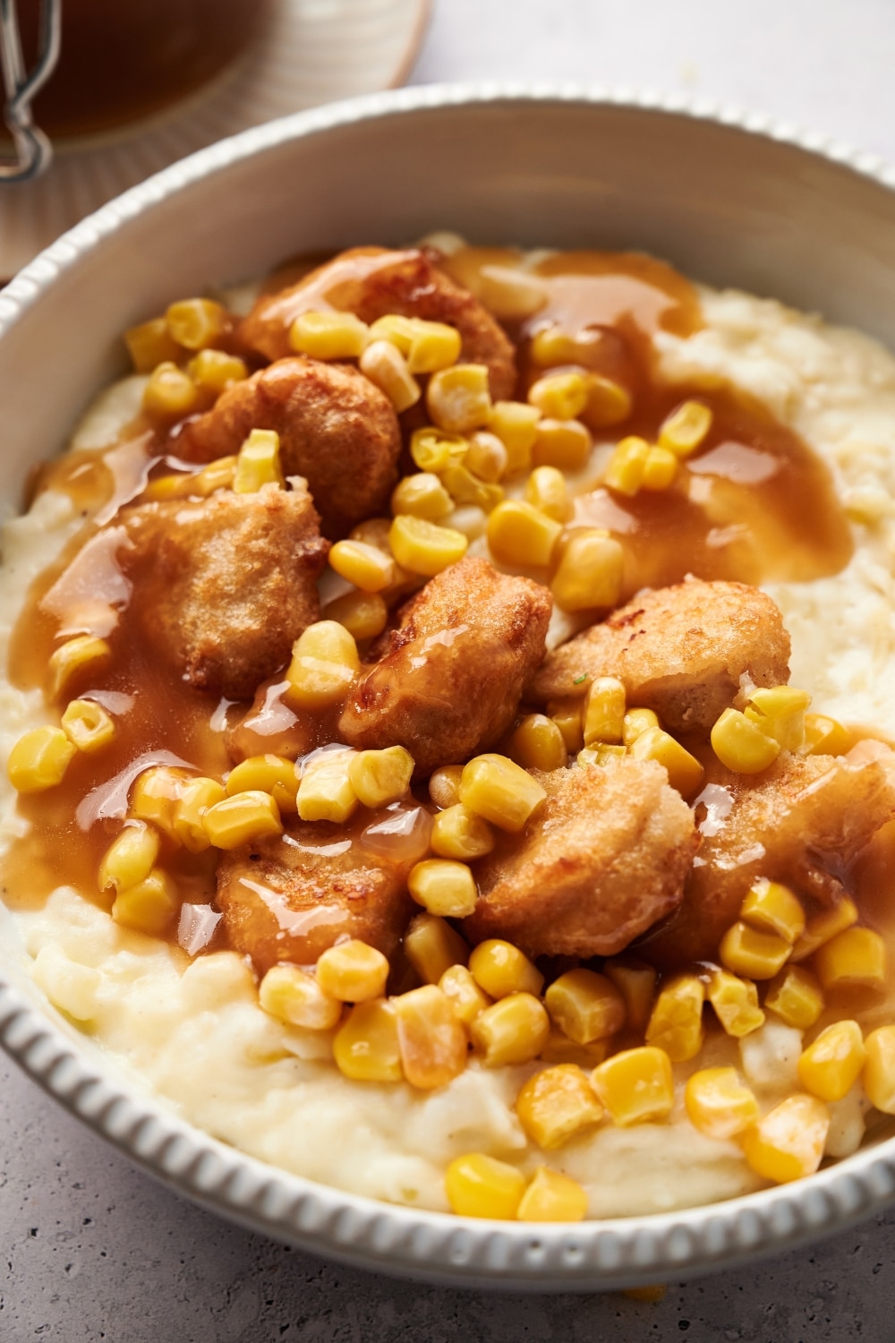 A KFC bowl filled with mashed potatoes, chicken nuggets, corn kernels, and brown gravy.