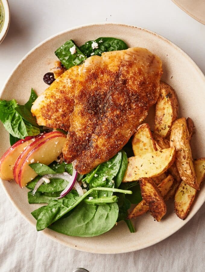 A piece of catfish on top of potatoes and spinach on a white plate.