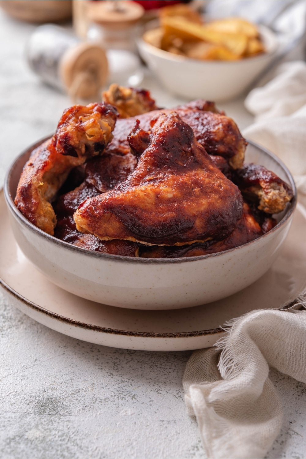 BBQ chicken wings in a white bowl on a white plate on a grey counter.