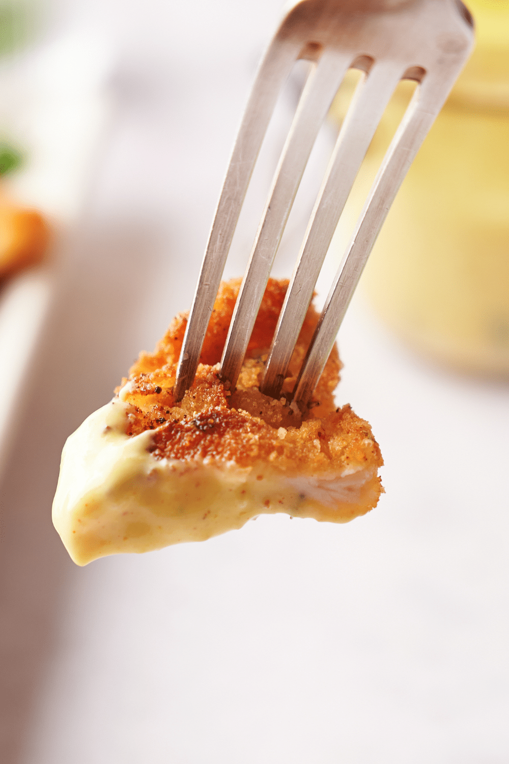 A fork holding a bite of breaded chicken coated in a yellow sauce.