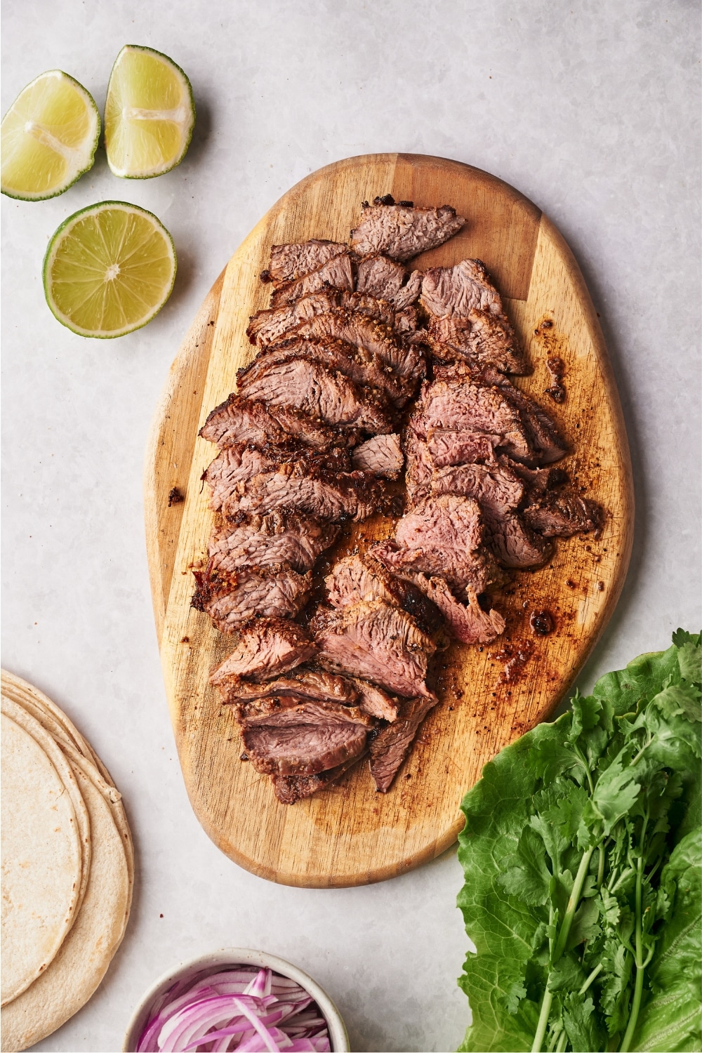 Sliced flank steak on a wooden cutting board on a grey counter.