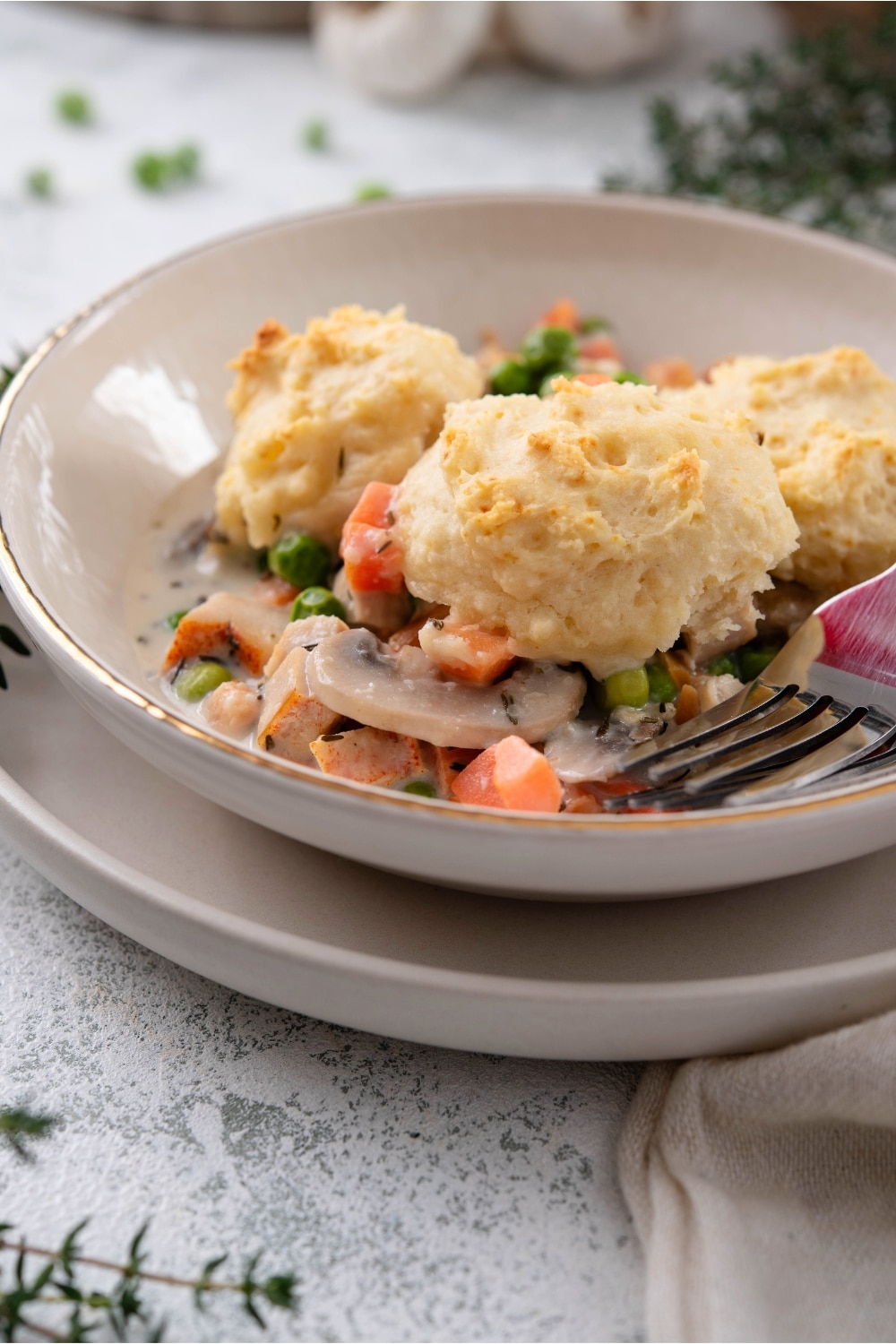 Part of a bowl with three biscuits on top of carrots, mushrooms, peas, and chicken in a creamy sauce.