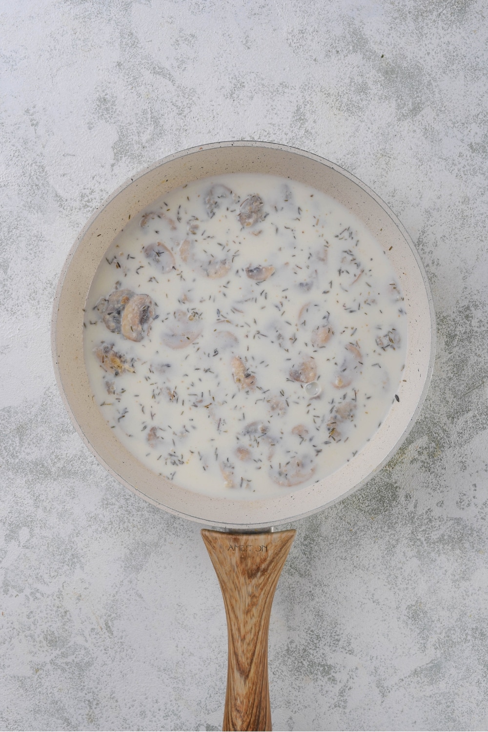 Mushrooms and seasonings simmering in a cream sauce in a white sauce pan.