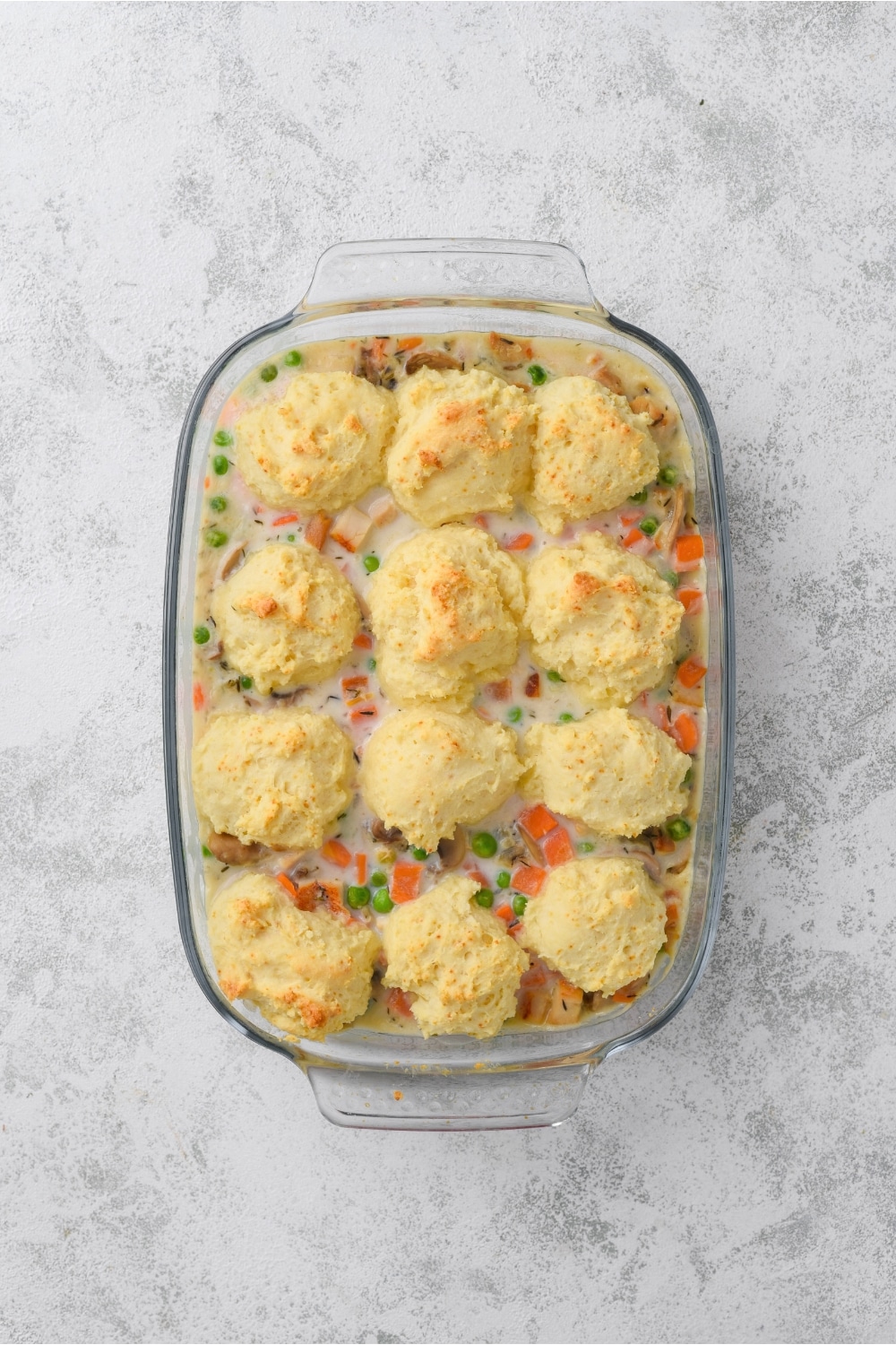 A glass casserole dish full of cooked chicken casserole. Twelve golden brown drop biscuits are on top.