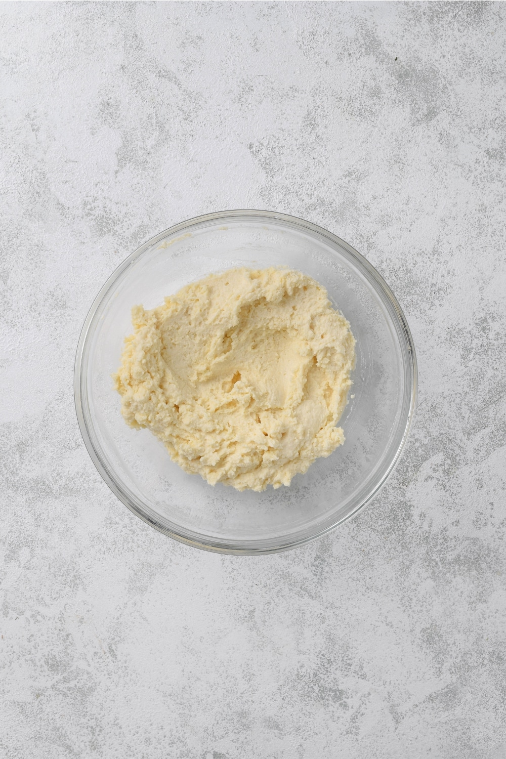 A glass bowl full of biscuit dough on a white counter.