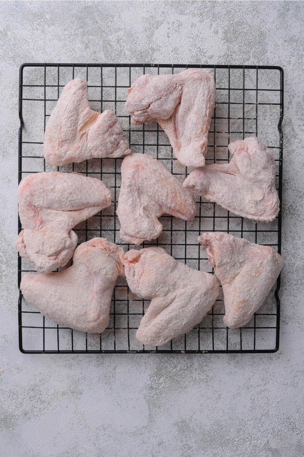 Raw chicken wings coated in flour on top of a wire rack on a counter.