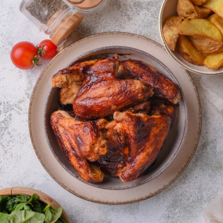 A bunch of bbq chicken wings in a bowl on top of a plate on a counter.