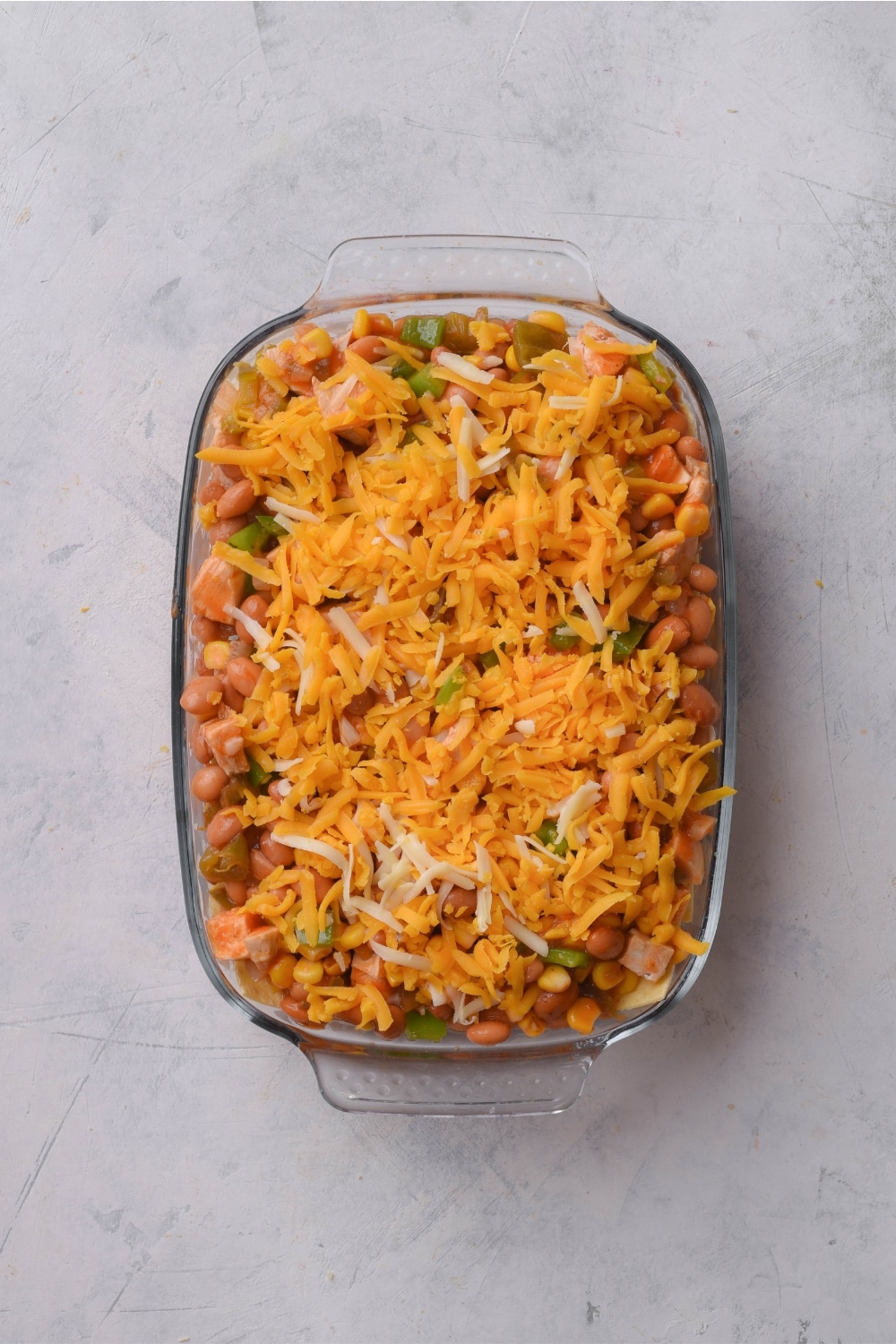 A baking dish filled with enchilada casserole covered in shredded cheese.