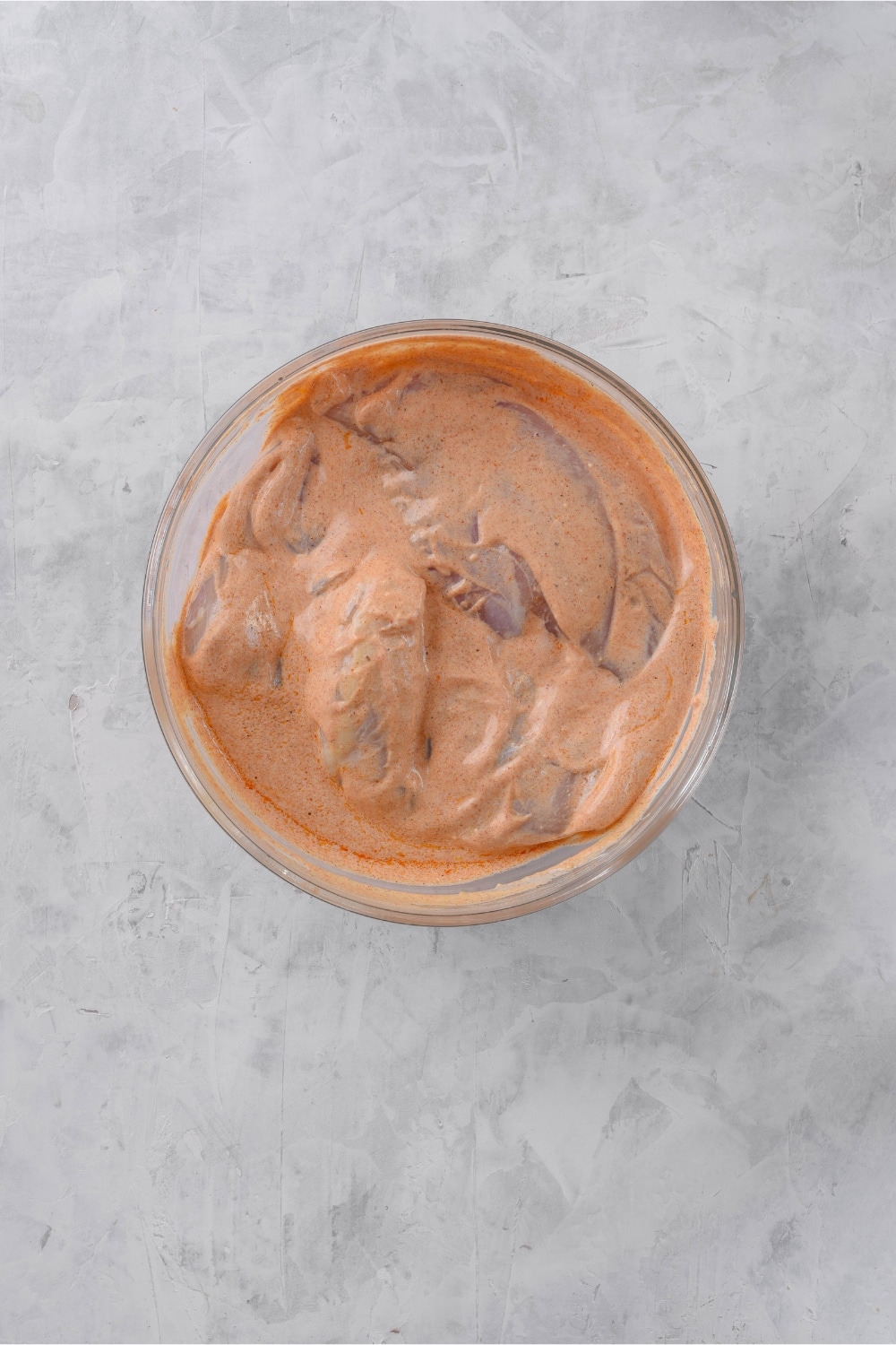 Chicken breasts coated in yogurt marinade in a glass bowl.