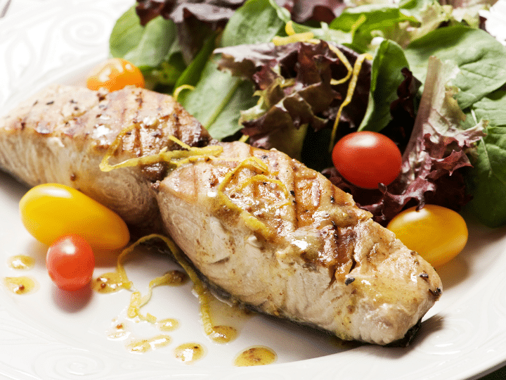 A piece of cooked mahi mahi on a plate with greens.