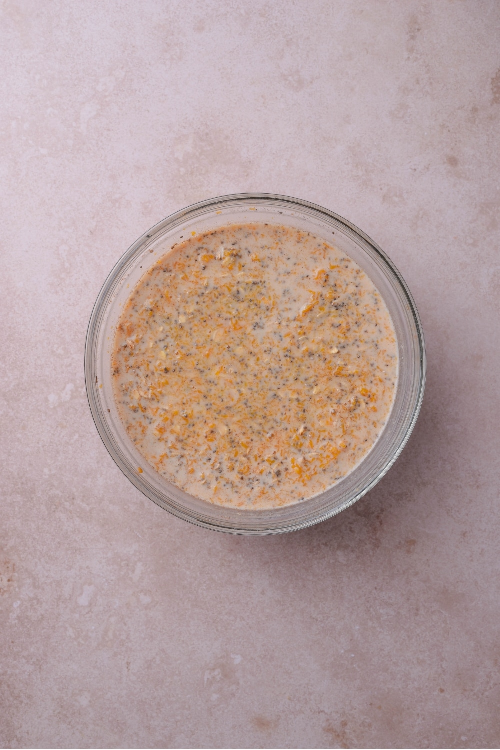 A glass bowl filled with oats, pumpkin, and chia seeds soaking in milk.