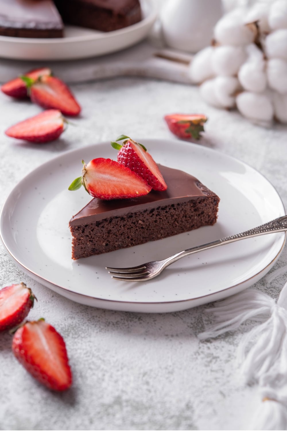 A slice of chocolate protein cake topped with sliced strawberries on a white ceramic plate. There is a fork next to the slice.