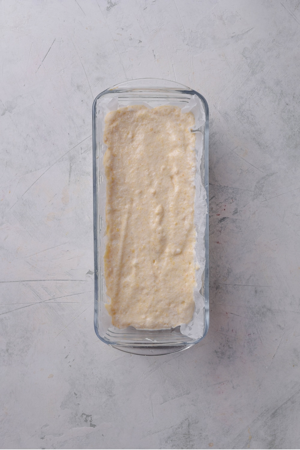An overhead shot of a glass loaf pan filled with raw protein bread dough.