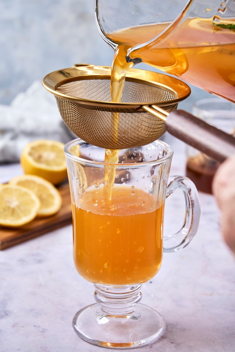 An image of flu bomb tea being poured from a glass pitcher through a small strainer into a glass tea mug.