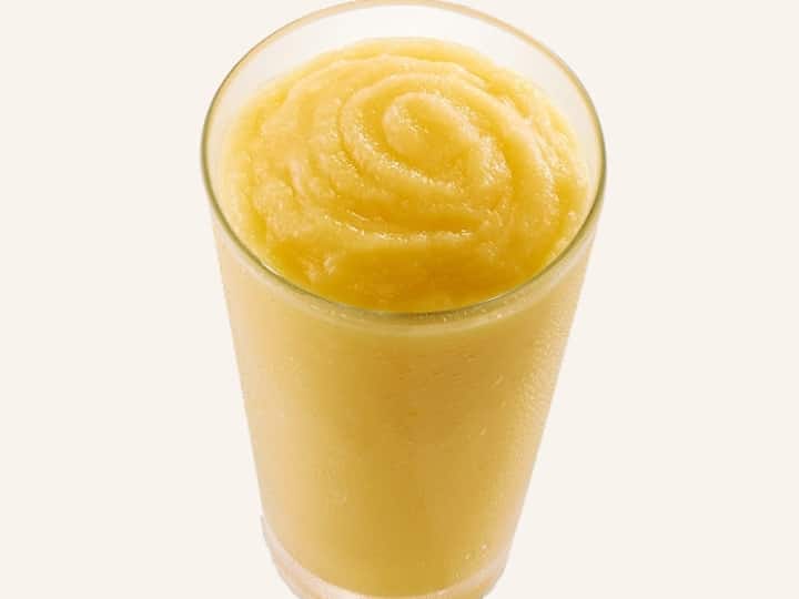 A yellow smoothie that is in a glass cup.