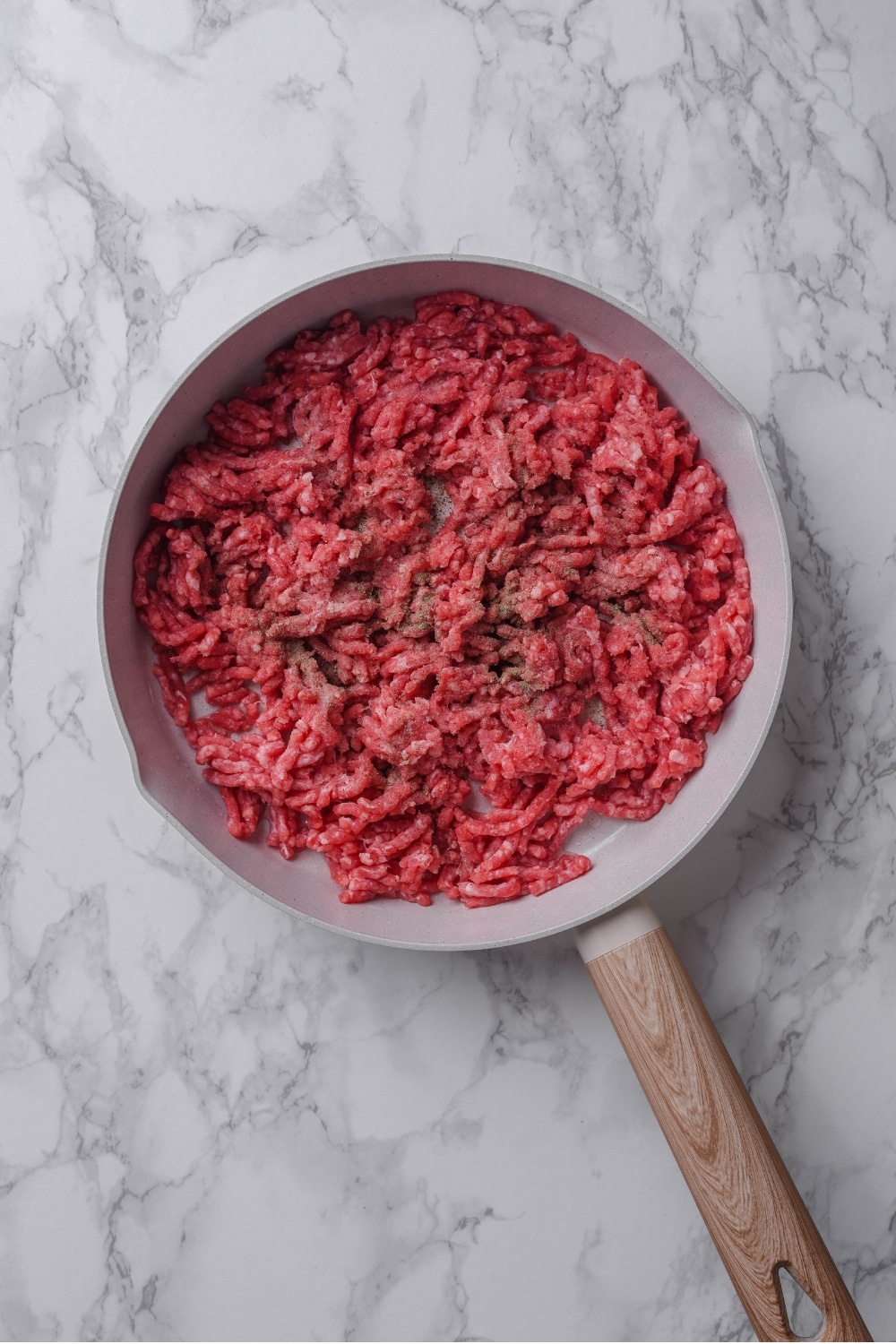 An overhead shot of a ceramic skillet with raw ground beef cooking in it.