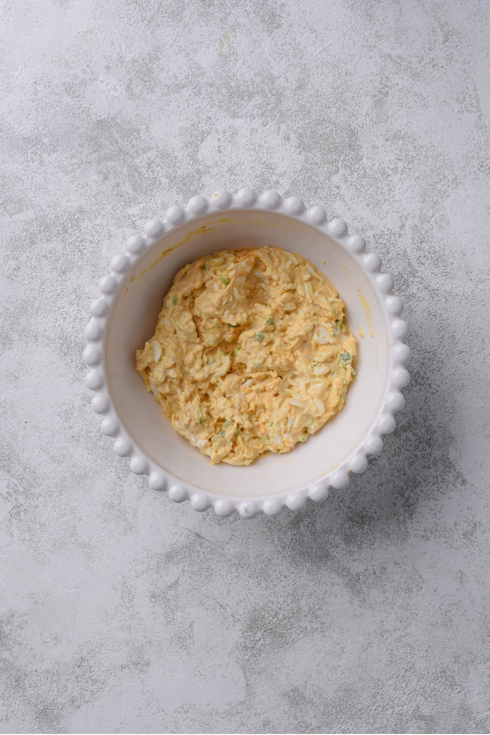 An overhead shot of a white porcelain bowl filled with an egg salad mixture.