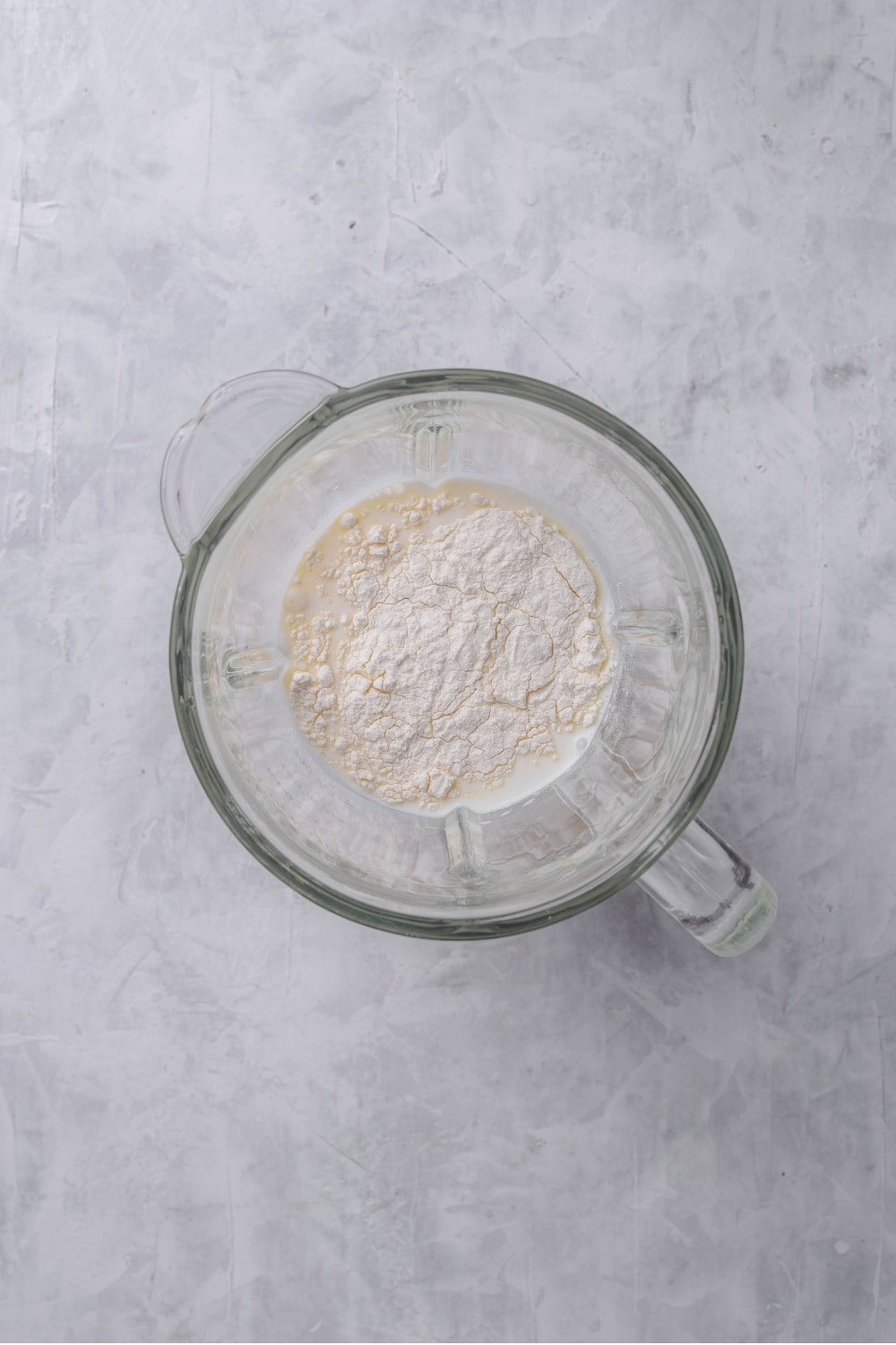 An overhead shot of a glass blender filled with milk, flour, and cream cheese.