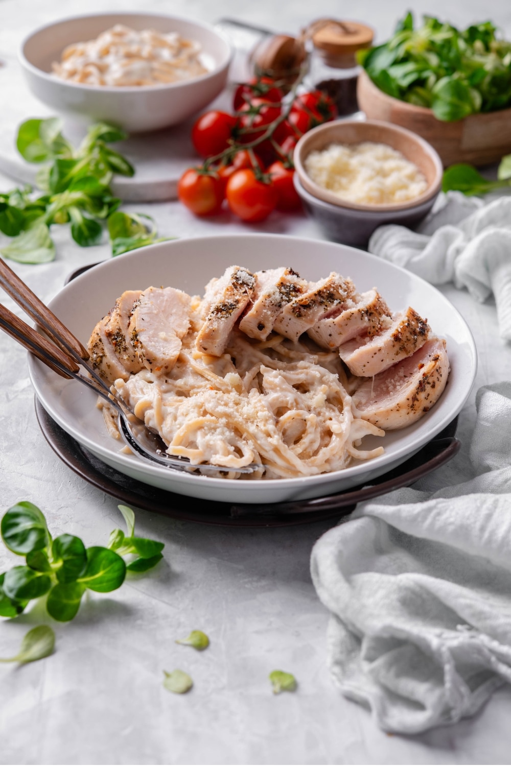 A ceramic plate filled with linguine in low calorie alfredo sauce, topped with sliced grilled chicken. There are two forks dipped into the pasta.