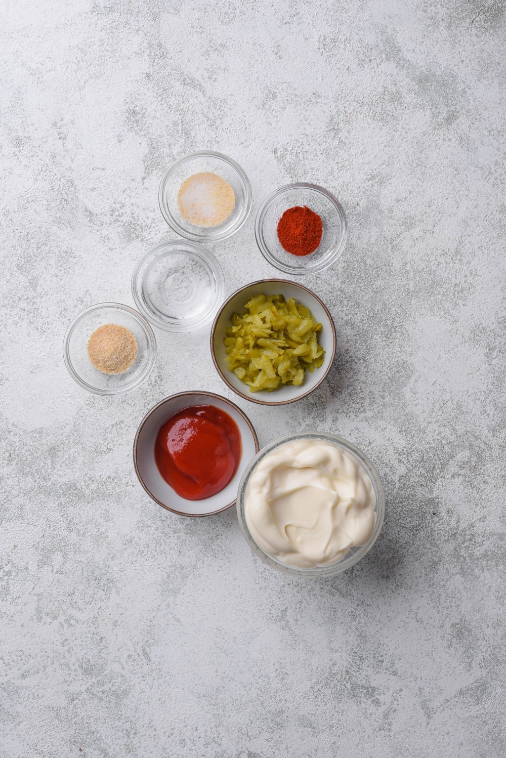 An overhead shot of several bowls filled with various ingredients for low calorie big mac sauce including mayo, ketchup, relish, vinegar, and spices.