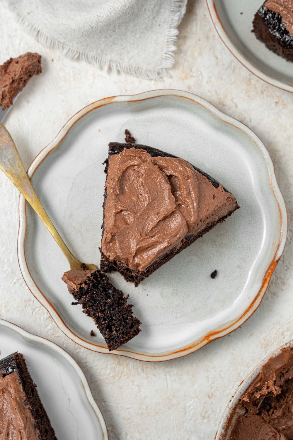 A slice of chocolate cake covered in chocolate frosting on a plate with a fork holding a bite of the cake.