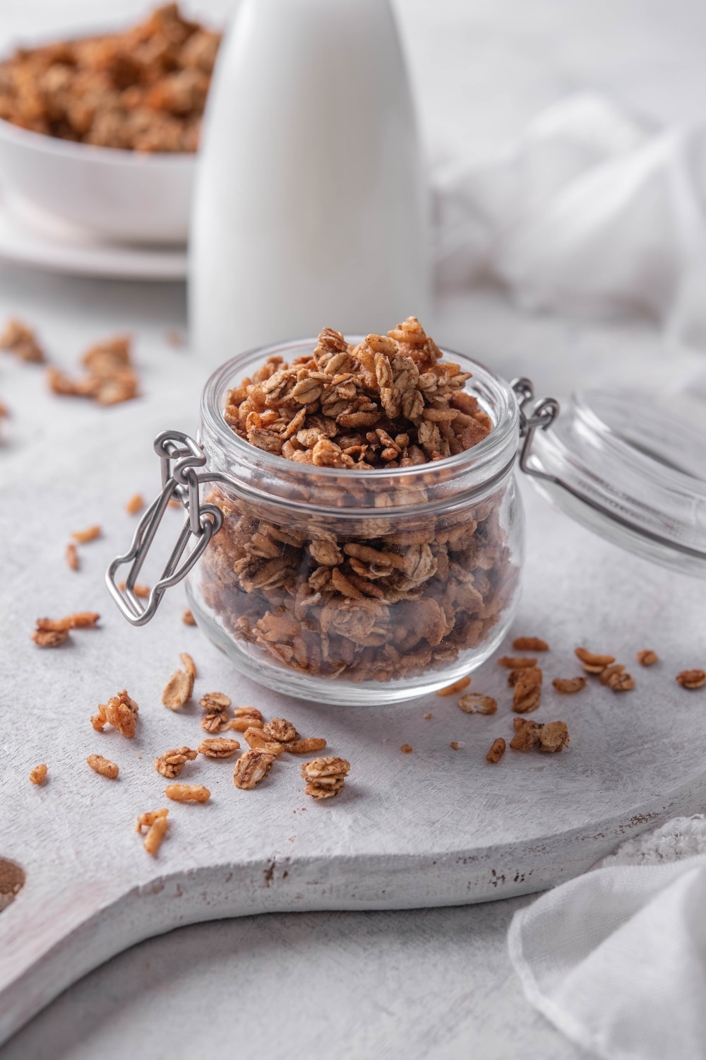 A clear jar filled with granola with pieces of granola spilling over the jar onto the counter.